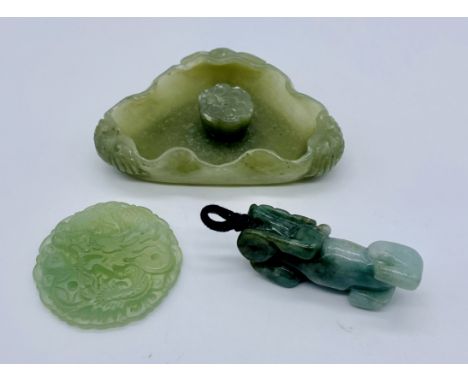Three pieces of carved jade. A temple lion pendant, an ornately carved round pendant depicting a dragon chasing a flaming pea