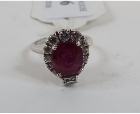 A white coloured metal ruby and diamond cluster ring, the central cushion cut ruby surrounded by brilliant and a baguette cut