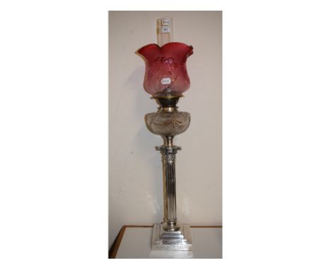 A late Victorian plated Corinthian column table oil lamp, with a cranberry glass shade and a cut glass reservoir, on a steppe