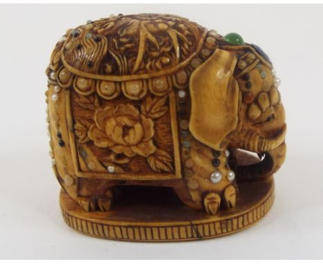 A Japanese ivory shibayama type netsuke, in the form of a caparisoned elephant, carved a dragon and flowers, set pearls and c