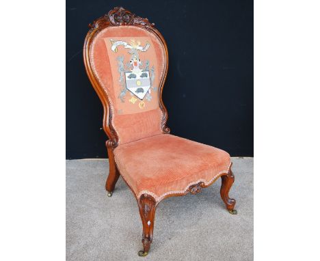 Victorian carved walnut nursing chair with tapestry armorial to the back, on cabriole legs and brass castors, 100cm high.