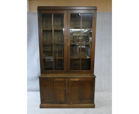 A mid century oak library bookcase with upper glazed section enclosing bookshelves above base fitted with panel doors on plin