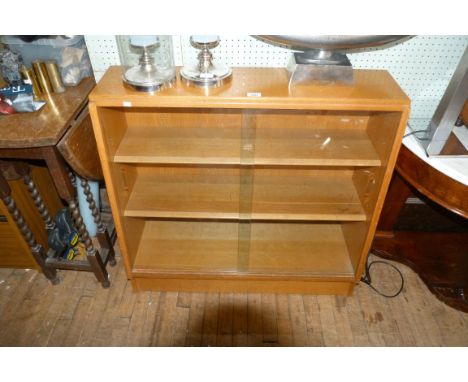 A mid Century light oak bookcase with twin sliding doors, enclosing two adjustable shelves.