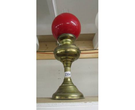 A brass oil lamp with red shade.
