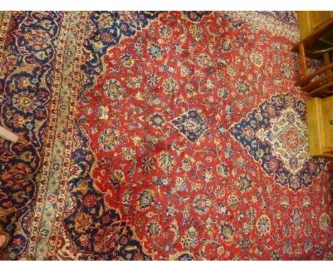 An Kashan carpet, with central floral medallion, surrounded by floral motifs, on a red and blue ground, contained by many flo