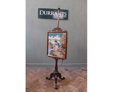 A Victorian walnut pole screen, with needlework panel, standing on a carved tripod base