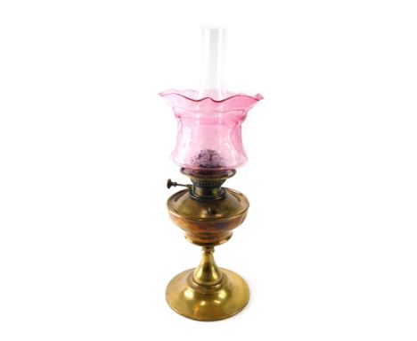 An early 20thC brass oil lamp, with clear glass funnel, brass reservoir and floral pink glass shade etched with flowers, shad