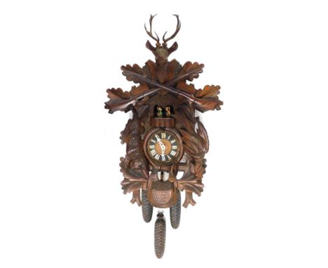 A Black Forest dancer and cuckoo clock, the pedimented case flanked by carved game, with stag finial and heavily carved leaf 