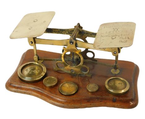 A set of Victorian brass postage scales, with some weights, on a shaped mahogany base, 20cm wide.