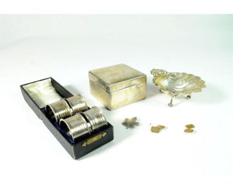 A cased set of four silver napkin rings, together with a silver mounted cigarette box, a silver shell butter dish, a pair of 