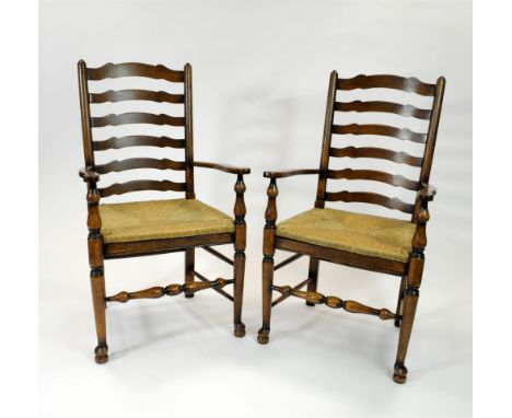 A pair of good quality reproduction stained oak rush seated leather back arm chairs, the ladder backs with shaped splats befo