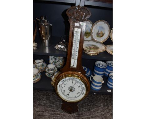 A carved oak wall mounted aneroid barometer.