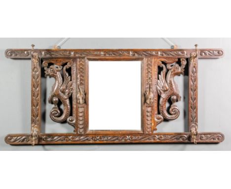 A late Victorian stained oak wall mirror and combined hat and coat hook, carved with two adorsed griffin supporters, and leaf