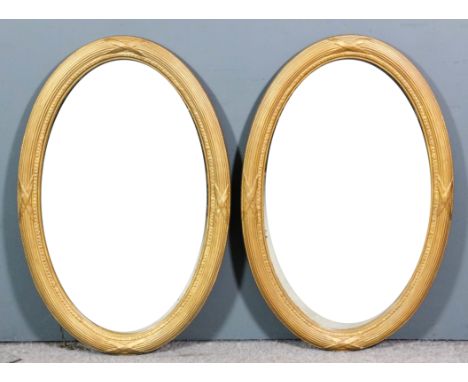 Two gilt wood oval wall mirrors with reeded and ribbon pattern frames, inset with bevelled mirror plates, each 34ins x 22ins 