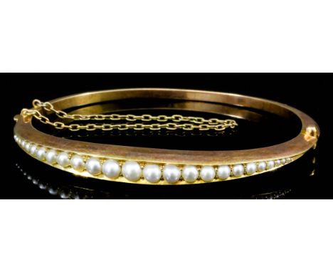 A late Victorian 15ct gold stiff bangle, the face set with twenty-four graduated seed pearls (gross weight 10.2 grammes)