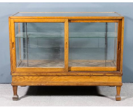 A 1930's oak framed and plate glass shop display counter, fitted one plate glass shelf enclosed by sliding glazed doors to re