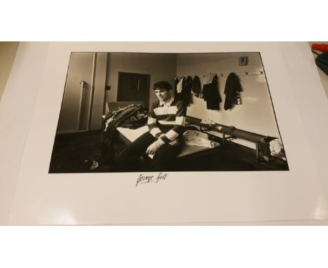 FOOTBALL, signed photo by George Best, half-length seated on bench in dressing room, 20 x 16, EX