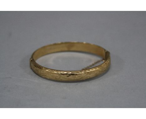A LATE 20TH CENTURY 9CT GOLD OVAL HINGED BANGLE, half engraved in a fancy scroll design, measuring approximately 66mm x 58mm 
