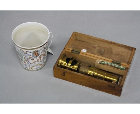 A CASED SMALL BRASS MICROSCOPE AND A QUEEN VICTORIA ENAMEL BEAKER (2)