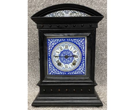 A 19th century aesthetic movement ebonised oak mantel clock with a blue and white enamelled dial and a bevelled glass door, a