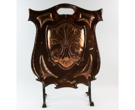  An Arts &amp; Crafts shield form copper fire screen, with hammered decoration, on wrought iron supports,  88 x 49 cm   .  