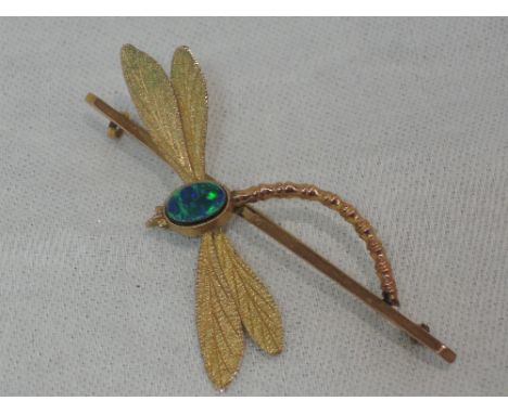 A yellow metal bar brooch stamped 9ct having an applique dragon fly with black opal doublet decoration