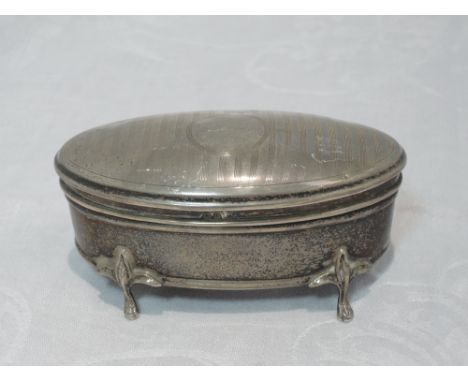 A silver dressing table box of oval form having engine turned stripe decoration, to hinged lid, trefoil paw feet and silk lin