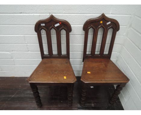 A pair of late Victorian oak hall chairs in the Gothic style having lancet backs with solid seats and bobbin legs