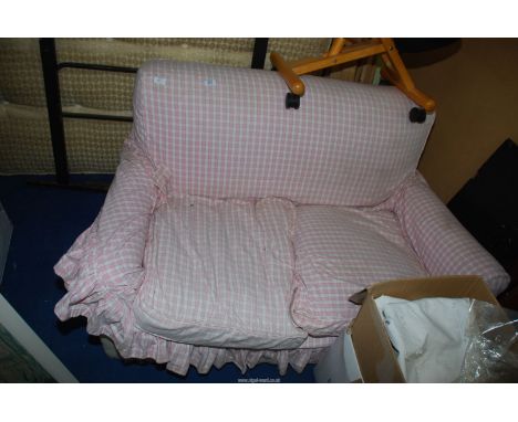 A small two seater sofa with pink and white cover.