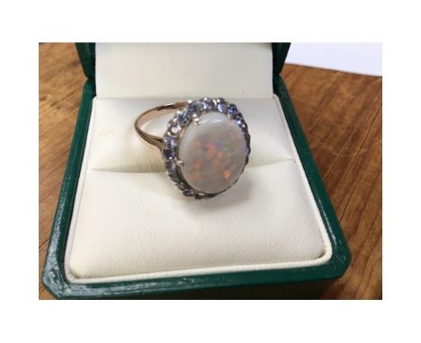 A 9ct yellow gold opal cluster ring. The centrally claw set oval shaped opal measuring 14 x 11mm, is surrounded by 22 x small