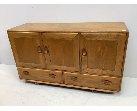 An Ercol light ash sideboard, with three panelled doors enclosing cutlery drawer and shelf, above two drawers, raised on cast