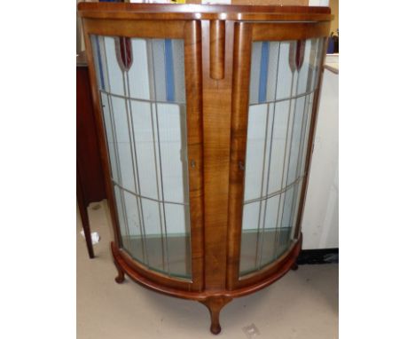 A 1930's walnut bow front side cabinet enclosed by leaded and coloured glass doors