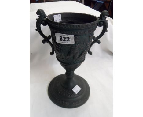 A cast metal two handled urn form cup decorated with cavorting putti with a bronzed verdigris finish