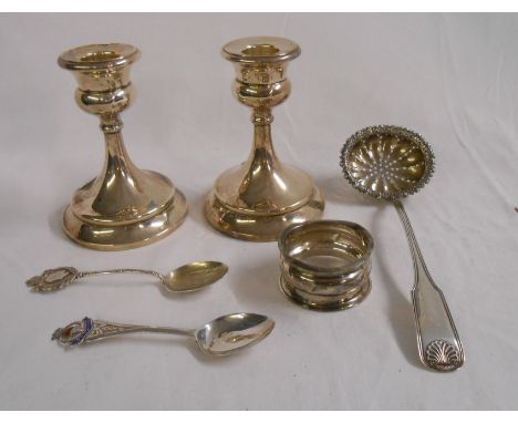 A pair of 11cm silver candlesticks - sold with a continental white metal sifter ladle, two silver souvenir spoons and a napki