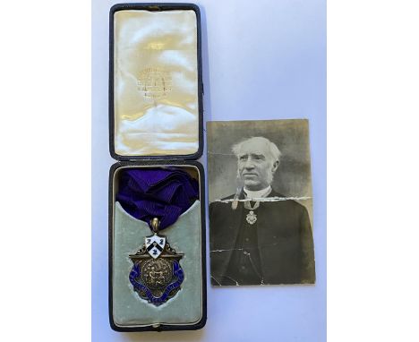 AN EDWARDIAN SILVER AND ENAMEL FRATERNITY BADGE. A Silver badge of rank with a central image of a man showing compassion to a