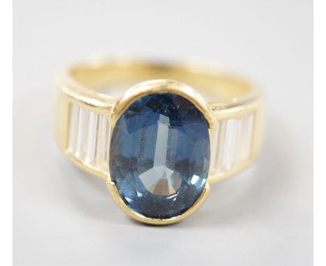 A modern 18ct gold and single stone oval cut sapphire set ring, with baguette cut diamond set shoulders, size R, gross weight