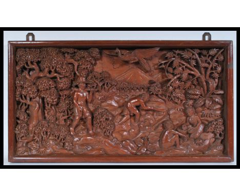 An early 20th century large carved wooden plaque depicting men at work amongst trees with children playing and bird over head