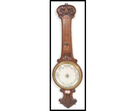 An early 20th Century Aneroid barometer set within a wooden case with carved floral decoration and inlaid thermometer dial. M