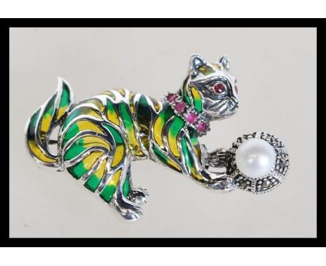 A sterling silver plique a jour brooch in the form of a cat playing with a ball having marcasite, pearl and red stone decorat