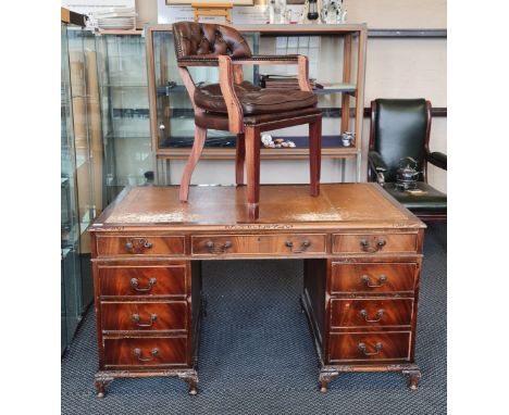 A mahogany reproduction desk together with a brown leather tub chair.