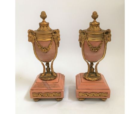 A pair of pink marble and ormulu, rams head and rose swag decorated urns with reversible top candlestick holders