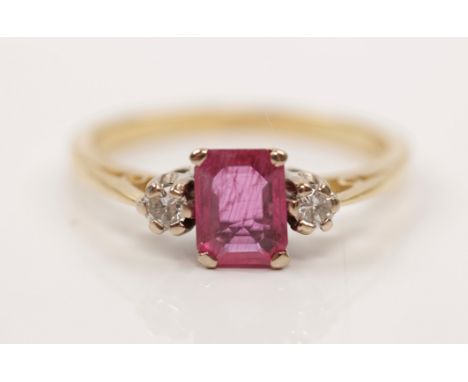 A hallmarked 18ct yellow gold ruby and diamond three stone ring, set with a central emerald-cut ruby (possibly treated), flan