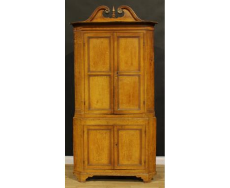 A 19th century pine floor-standing corner cupboard, scumbled as oak, swan neck pediment above a pair of panel doors enclosing