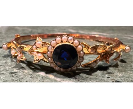 A late 19th/early 20th century 15ct gold hinged bangle bracelet, set with a central synthetic sapphire accented with seed pea