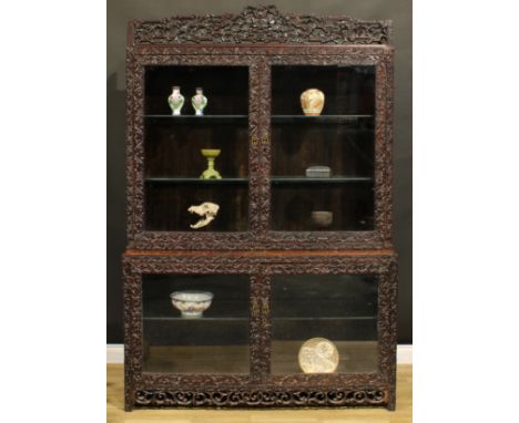 A Chinese hongmu porcelain vitrine or display cabinet, shaped pediment pierced and carved with meandrous leaves and stylised 