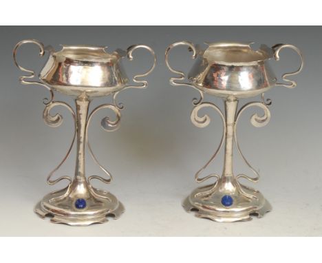 A pair of Art Nouveau silver pedestal cups, shaped borders, sinuous whiplash handles and supports, lightly planished overall,