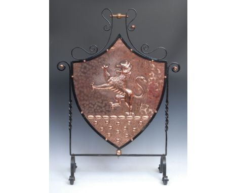 An Arts and Crafts beaten copper and wrought iron armorial fire screen, the shield shaped panel embossed with a heraldic cres