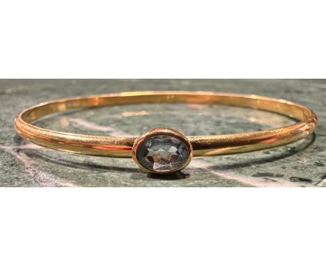 A pale blue topaz set indistinctly marked gold bangle, rounded body set with a single blue oval topaz, approx 7.5mm x 5.3mm x