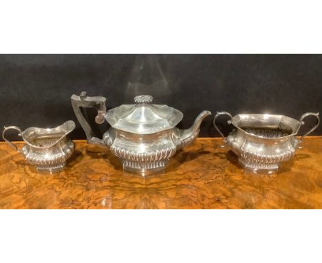 An Edwardian silver half fluted three piece tea service, comprising teapot, sugar basin and cream jug, the teapot with ebonis