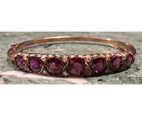 A ruby and diamond hinged bangle, the seven graduated oval facet cut stones divided by pairs of diamond chips, 5.7cm internal